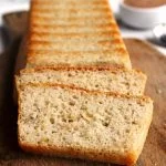 Pão de forma sem glúten fatiado sobre tábua de madeira em uma mesa branca