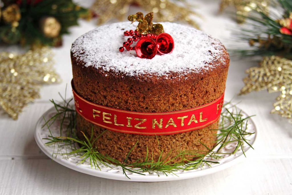 Panetone decorado com açúcar confeiteiro, fita vermelha e enfeites natalinos
