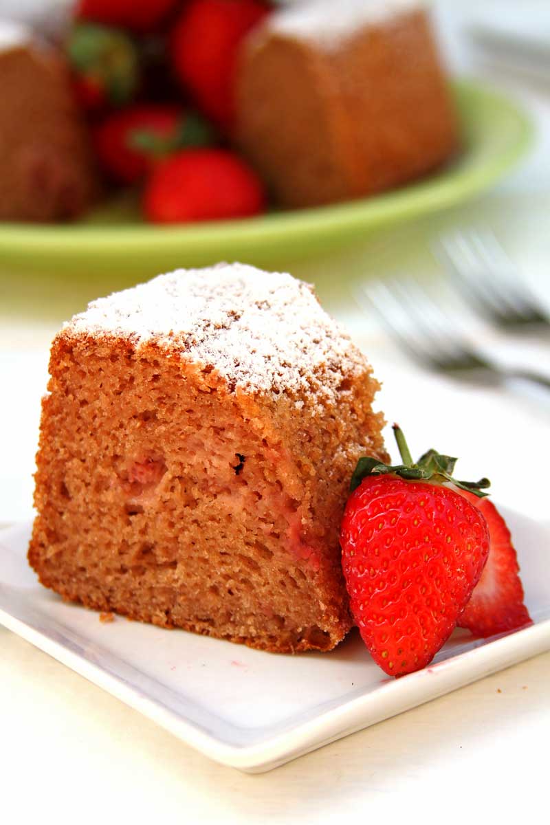pedaço de bolo de morango com um pouco de açúcar confeiteiro por cima e decoração de morango natural