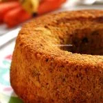 Bolo de banana com cenoura redondo com furo no meio sobre prato colorido em mesa branca