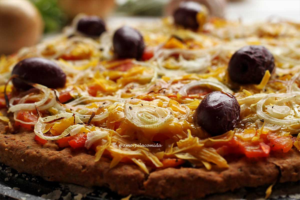 Pizza caseira sobre pedra de pizza com molho de tomate, queijo vegano, cebola e azeitonas pretas