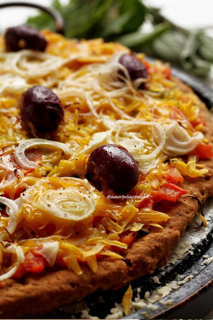 Pizza de queijo com tomate, cebola e azeitonas pretas sobre pedra de pizza em mesa branca