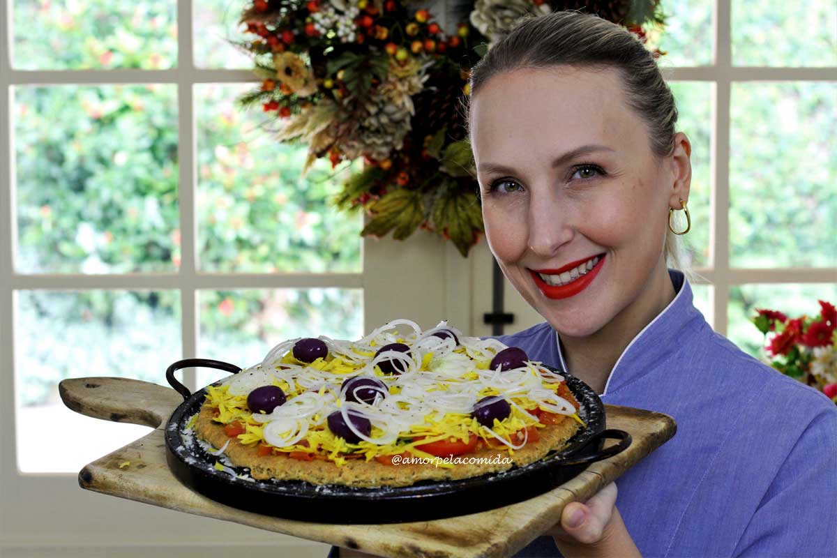Mulher branca loira segurando tábua de madeira com pizza em uma forma de pedra