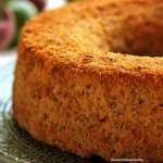 Bolo de limão redondo com furo no meio sobre prato verde escuro em uma mesa branca com batata-doce e limões ao fundo