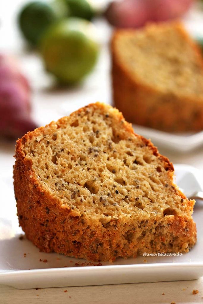 Duas fatias de bolo de limão fofinho sobre prato quadrado pequeno em uma mesa branca com batata-doce e limões ao fundo