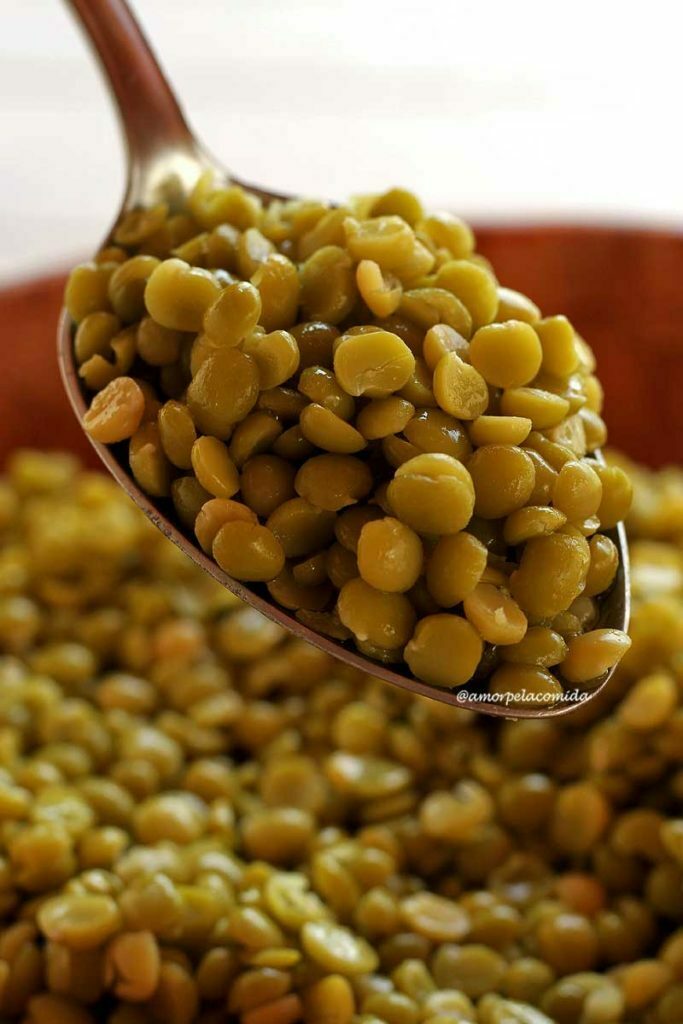 COMO COZINHAR ERVILHA SECA SEM PANELA DE PRESSÃO Colher cheia de ervilha cozida sobre bacia de bambu, dentro da bacia mais grãos de ervilha cozidos
