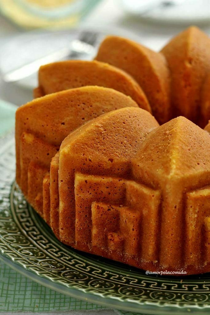 BOLO DE FUBÁ DE LIQUIDIFICADOR FIT Bolo redondo com furo no meio assado em uma forma com padrões geométricos, lembrando arte deco