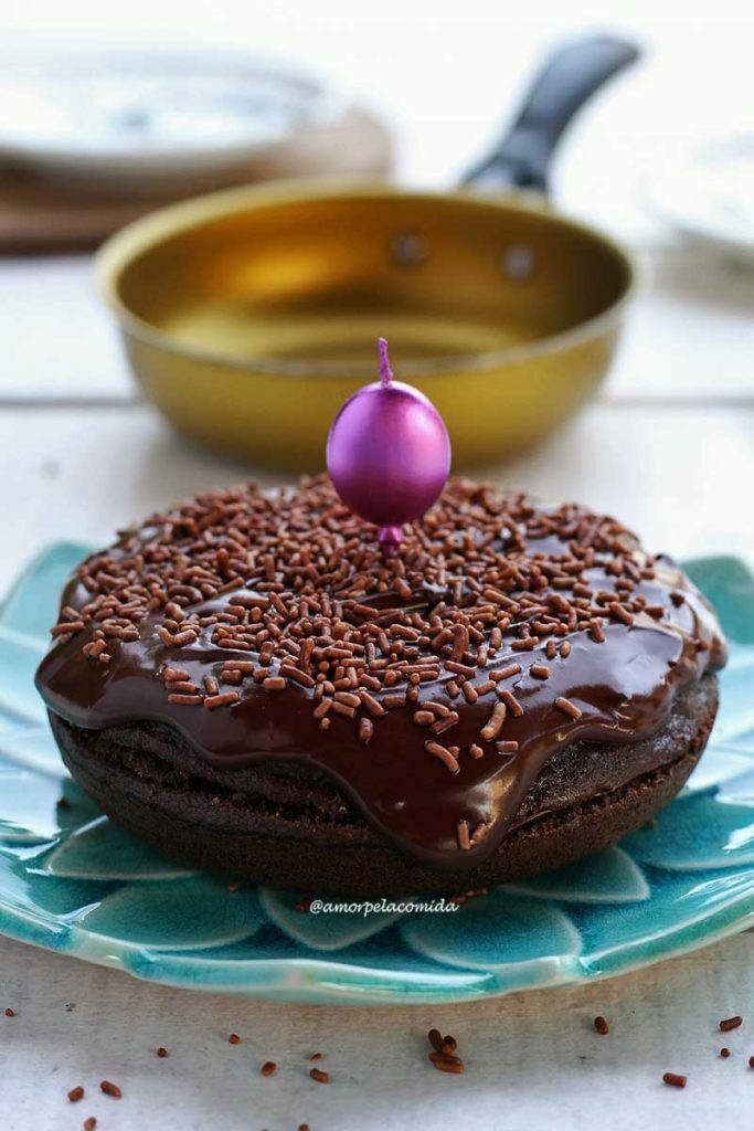 BOLO DE FRIGIDEIRA SEM FARINHA DE TRIGO Bolo de chocolate redondo pequeno sobre prato azul turquesa, ao fundo uma frigideira amarela desfocada