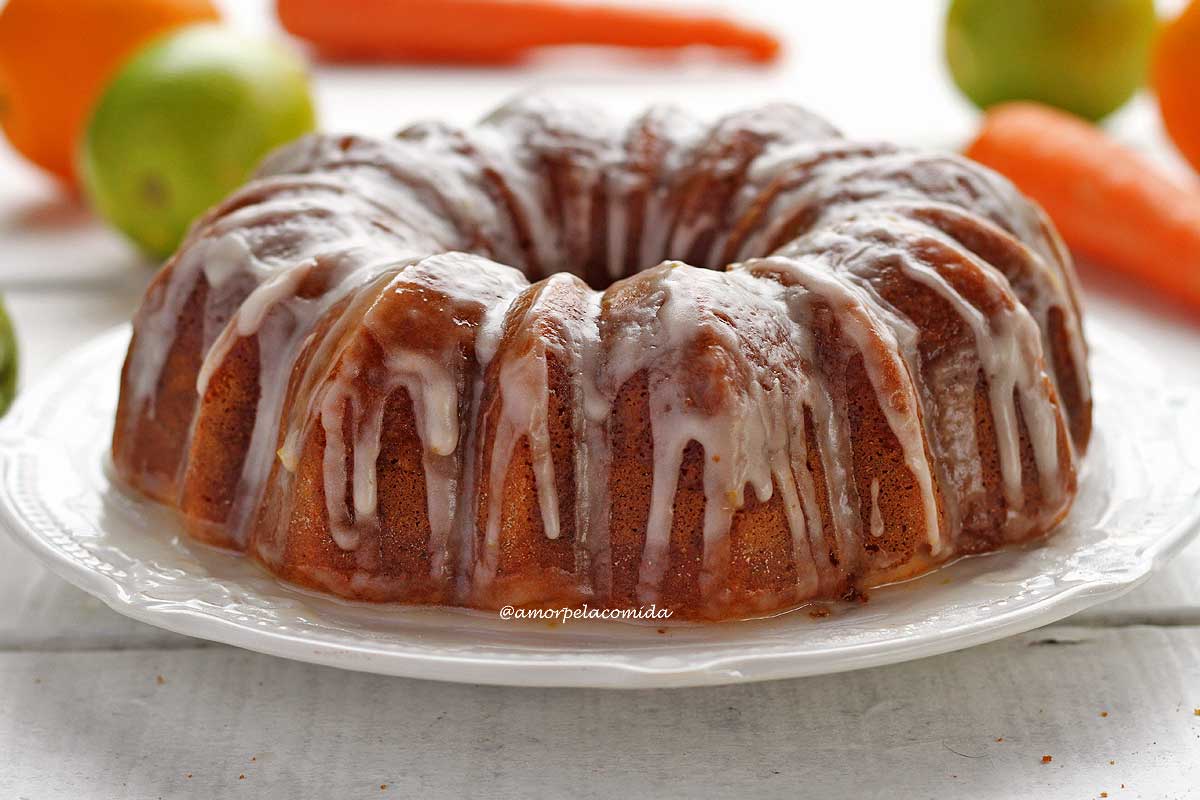 Bolo de cenoura com laranja redondo com furo no meio coberto de glacê de açúcar sobre um prato branco