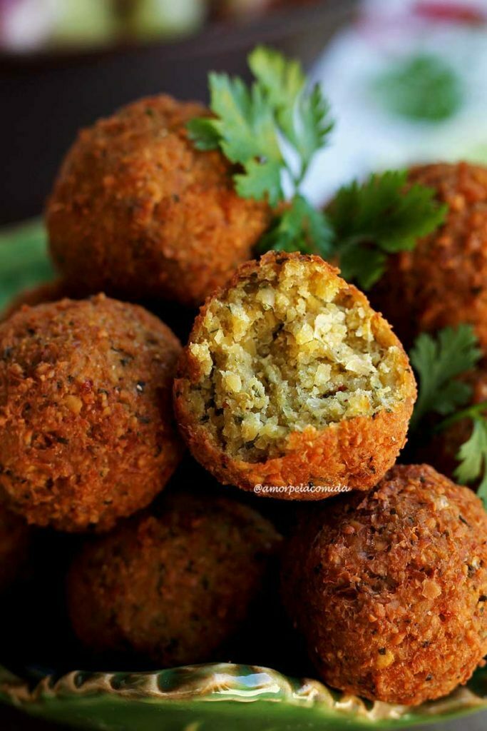 FALAFEL VEGANO vários bolinhos de grão-de-bico amontoados em uma tigela verde, decorados com ramos de coentro fresco