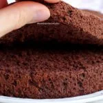 Bolo pão de ló cortado ao meio, mão levantando a fatia de cima para mostrar a textura aerada da massa