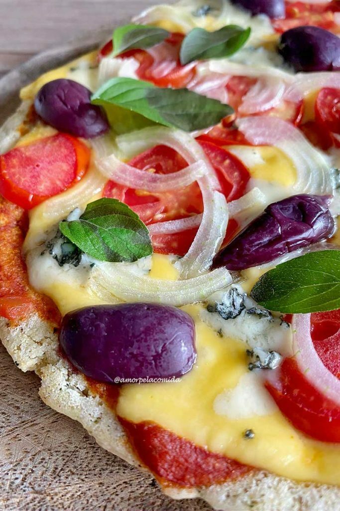 PIZZA DE FRIGIDEIRA FIT CROCANTE Pizza sobre tábua de madeira, na cobertura queijo, tomate, cebola, manjericão e azeitonas pretas