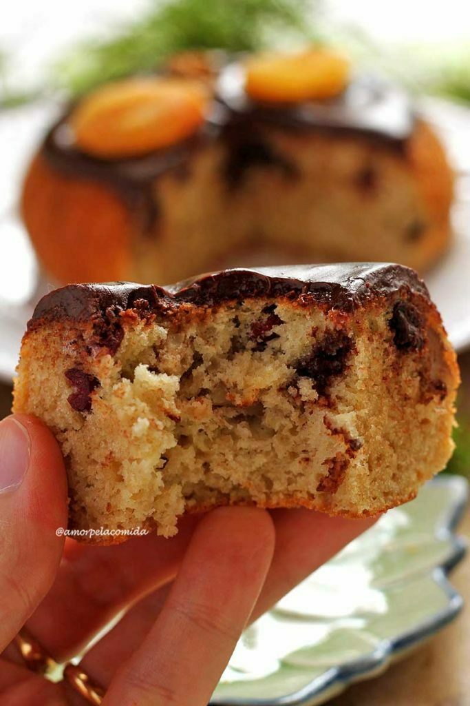 Mão segurando pedaço de panetone mordido mostrando a textura macia da massa e cremosa da cobertura de chocolate