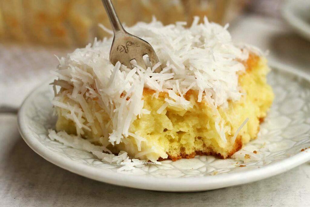 Pedaço de bolo de coco com cobertura de coco com garfo partindo o bolo e mostrando a textura macia e úmida da massa