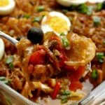 Travessa de vidro transparente com bacalhau com batatas, cebola, azeitonas, pimentões coloridos, ovo e cebolinha verde