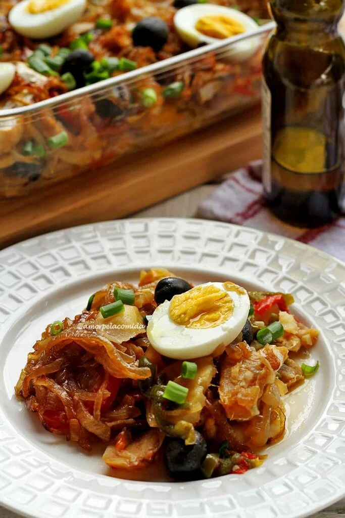 Prato branco redondo com bacalhoada dentro, diversos vegetais e por cima metade de um ovo cozido