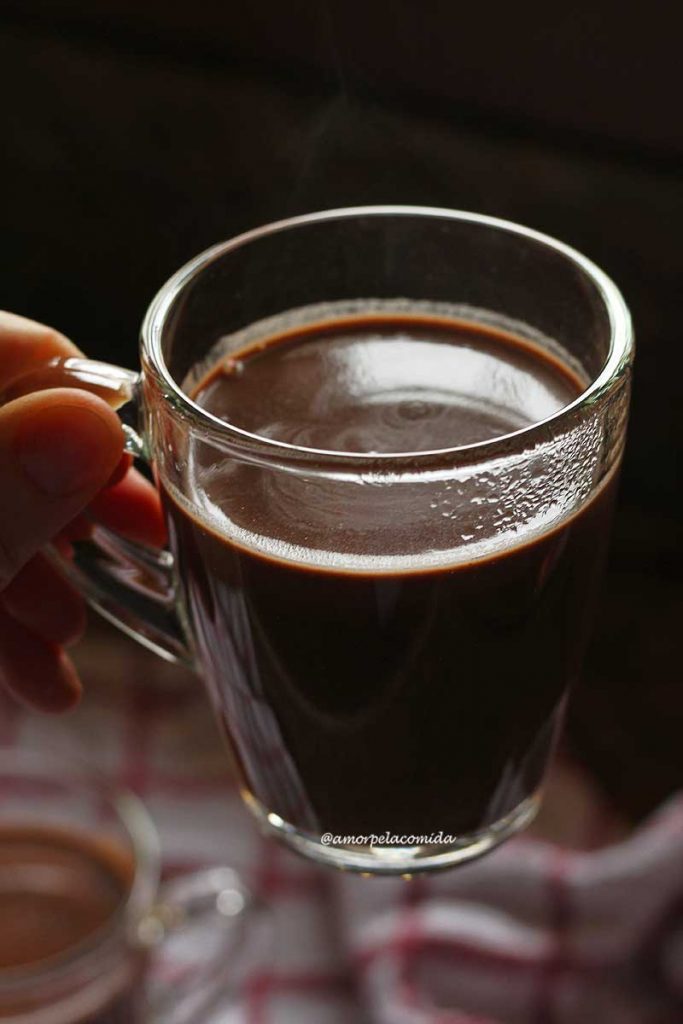 Mão segurando xícara de vidro transparente com chocolate quente dentro