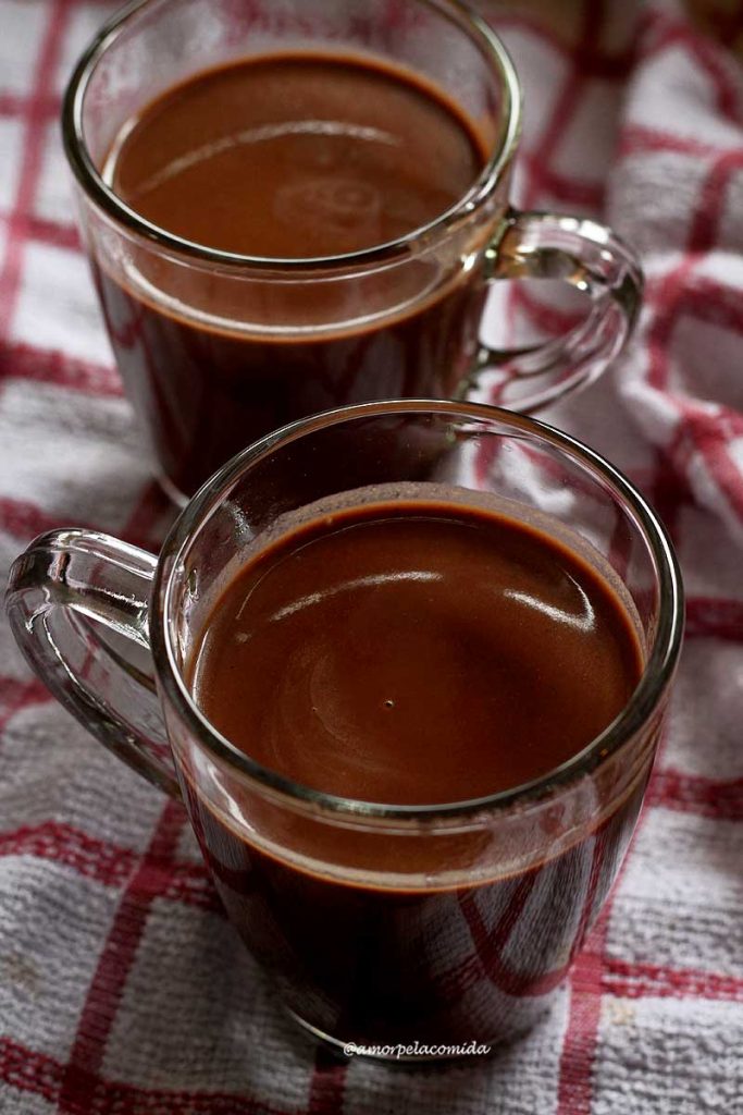 Duas xícaras de chocolate quente sobre pano branco e vermelho quadriculado