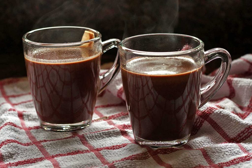 Duas xícaras de chocolate quente sobre pano branco com quadriculado vermelho
