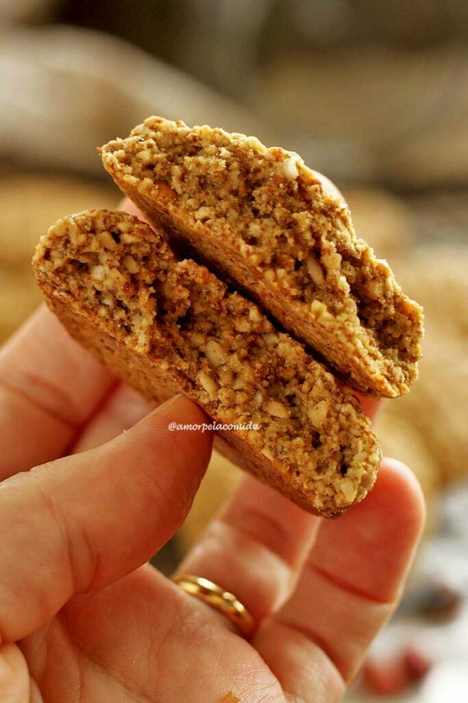 Mão segurando um biscoito de amendoim partido ao meio mostrando a textura interna levemente aerada