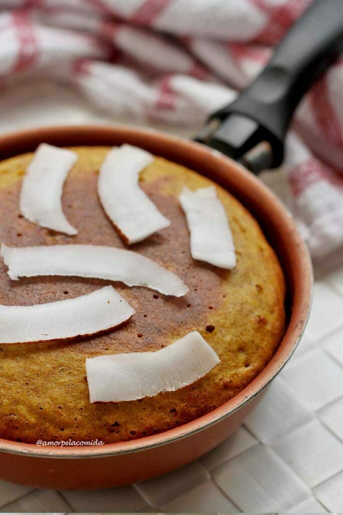 Frigideira pequena com bolo de abóbora com coco dentro, por cima lâminas de coco fresco