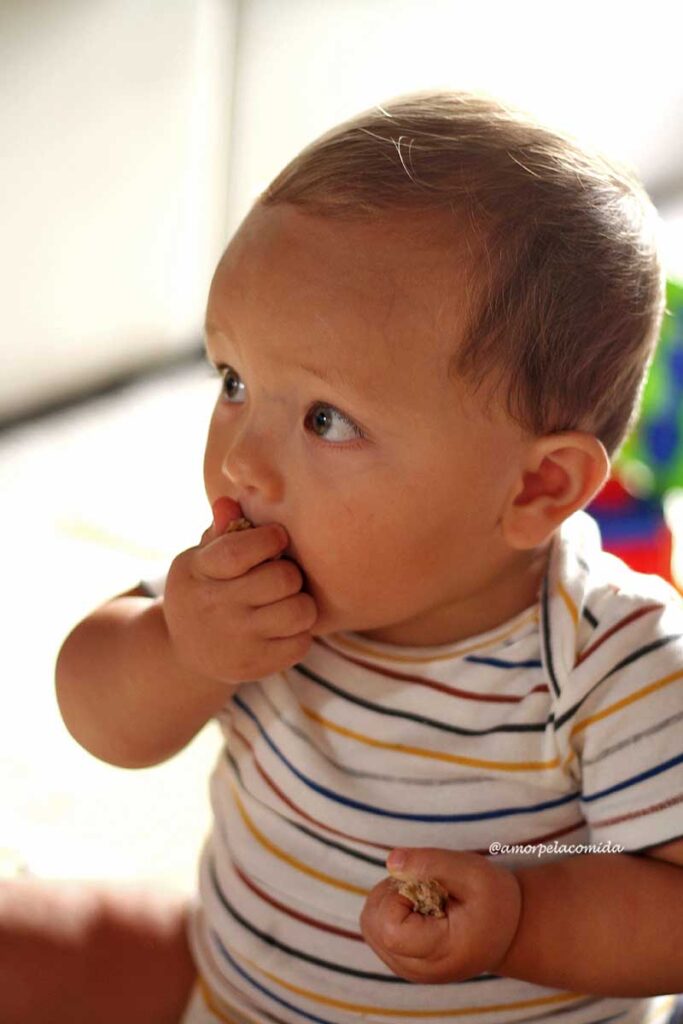 Bebê de 10 meses comendo bolo de banana, levando a mão até a boca