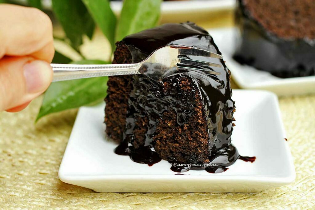 Mão segurando garfo pequeno de metal que está pressionando a fatia de bolo de chocolate para tirar um pedaço