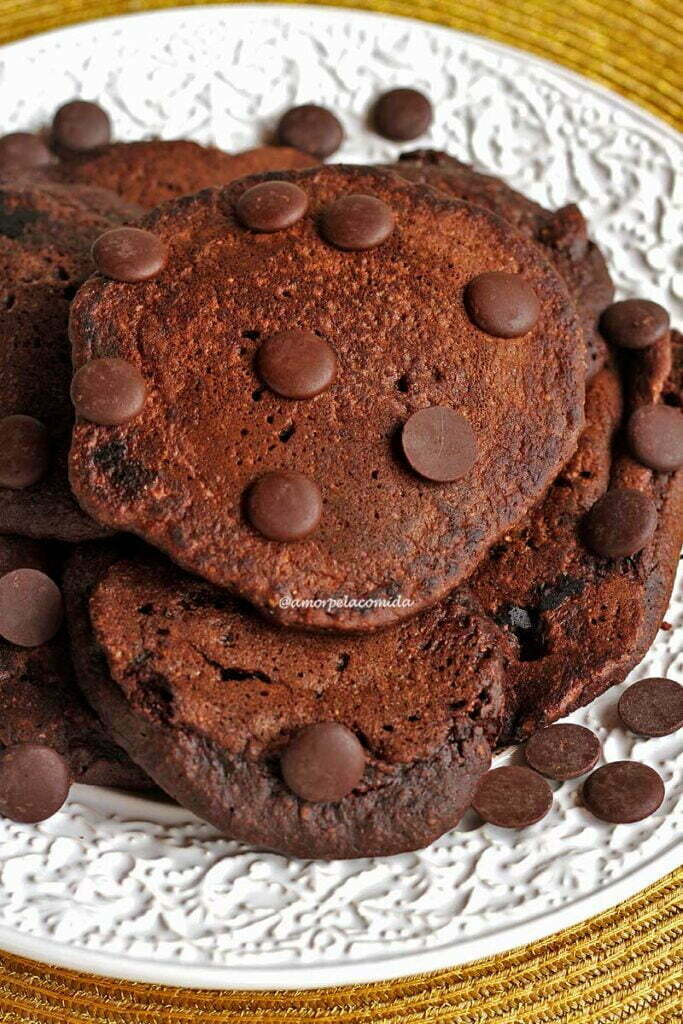 PANQUECA AMERICANA DE CHOCOLATE SEM TRIGO SEM LACTOSE Várias panquecas de chocolate amontoadas sobre prato branco, sobre as panquecas gotinhas de chocolate para enfeitar
