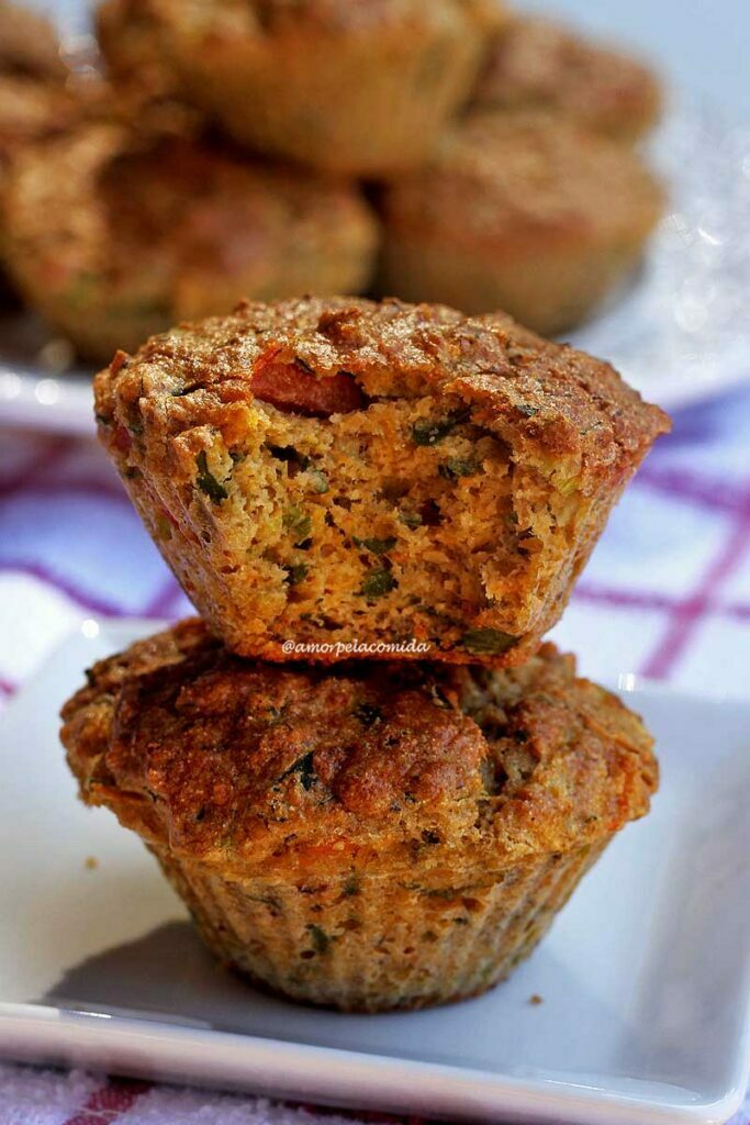 Dois muffins salgados empilhados, o de cima está mordido mostrando pedacinhos de espinafre e tomate