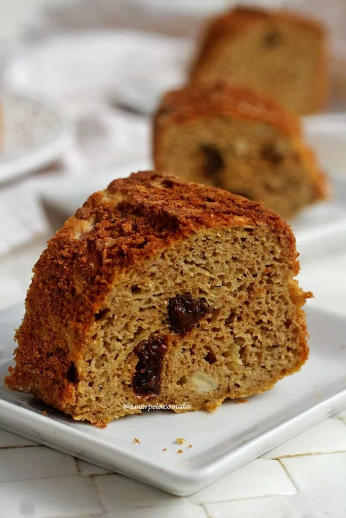 Três fatias de bolo alinhadas em uma mesa branca, cada uma está em um prato quadrado pequeno