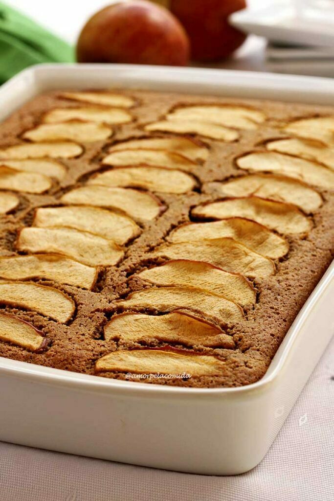 Forma de bolo retangular grande com bolo de maçã dentro que no topo tem várias fatias finas de maçã que estão levemente douradas