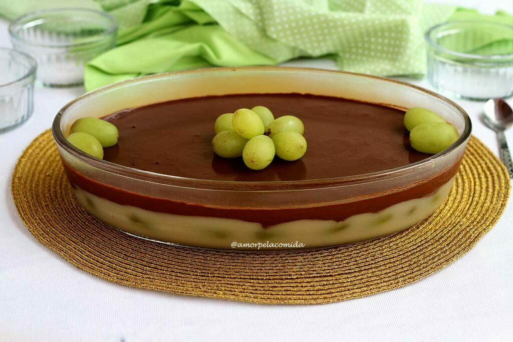 Travessa oval de vidro com uma sobremesa em duas camadas, a camada de baixo é um creme branco com uvas verdes e por cima uma cobertura cremosa de chocolate