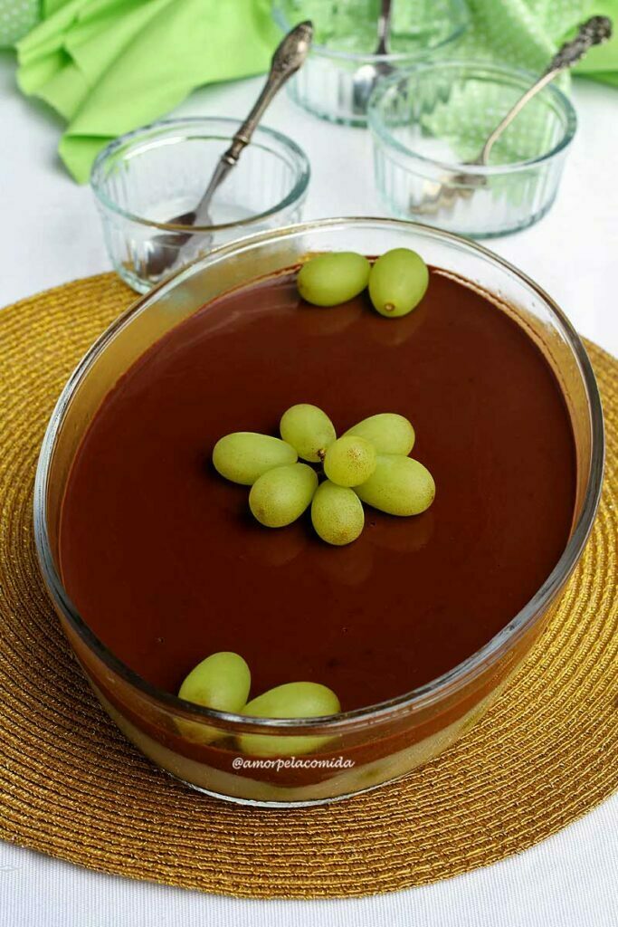 Travessa oval com sobremesa de uva, no topo chocolate cremoso e algumas uvas decorando