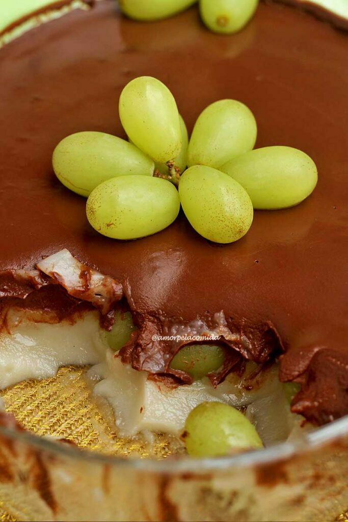 Travessa de vidrol oval com sobremesa de uva dentro, por baixo o creme de baunilha, no meio a uva verde e por cima chocolate cremoso