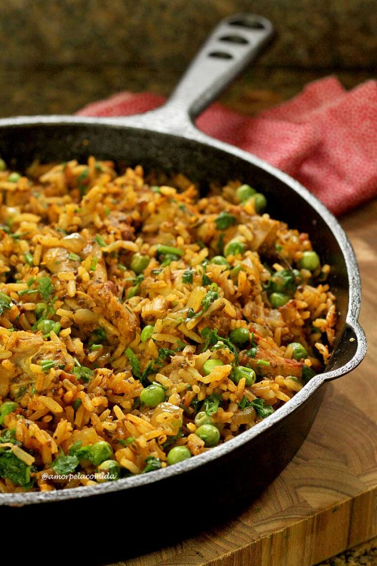 Caçarola de ferro fundido sobre tábua de madeira, dentro frango com arroz e ervilha mais temperos