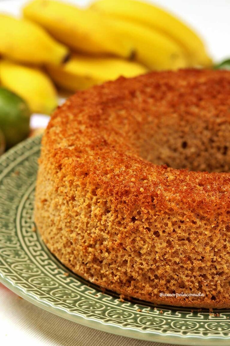RECEITA DE BOLO DE BANANA COM AVEIA SEM AÇÚCAR SEM ADOÇANTE Bolo redondo com furo no meio sobre prato verde, ao fundo um cacho de banana e uns limões