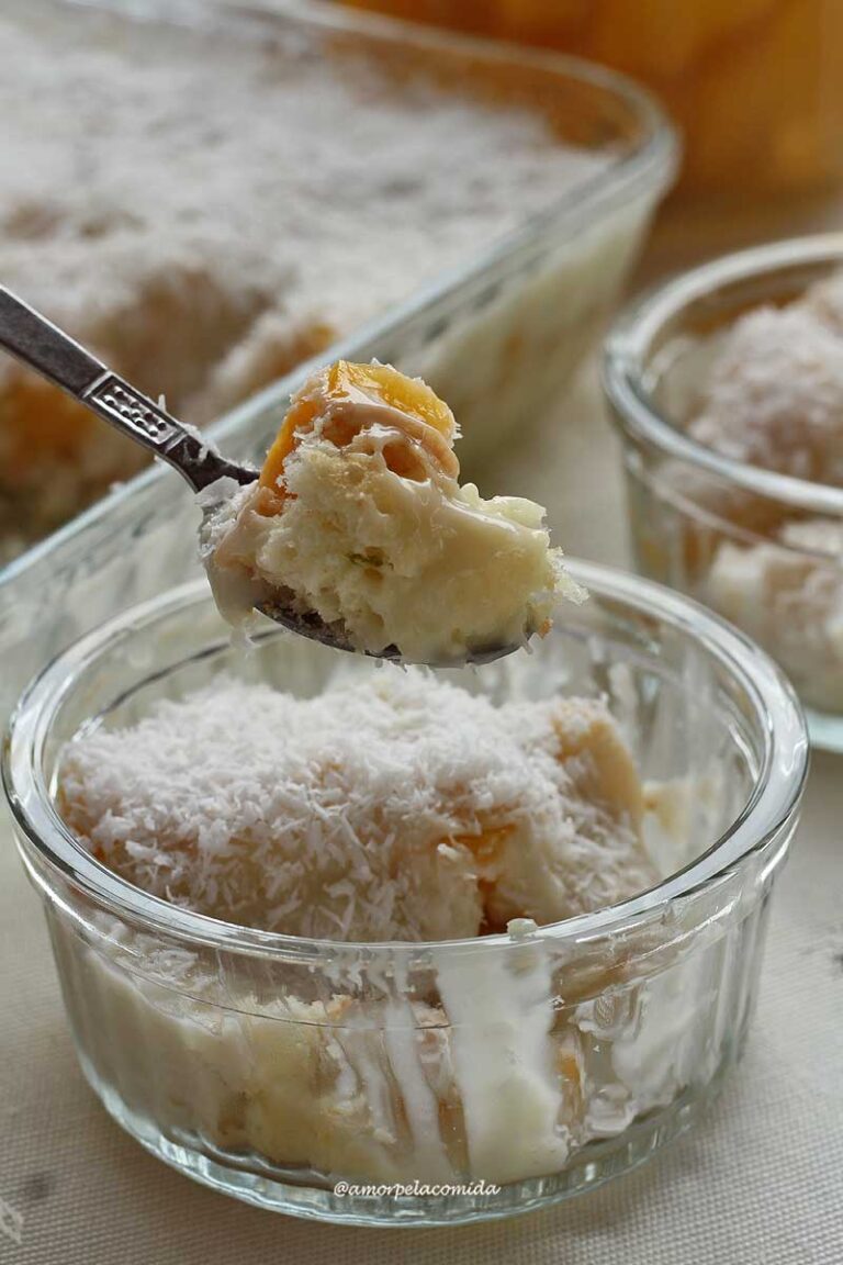 Colher pequena servindo uma porção de sobremesa de pêssego, abaixo o potinho da sobremesa, ao fundo uma parte da travessa