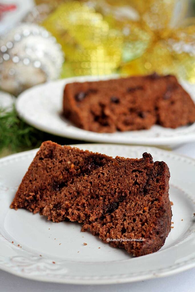 Duas fatias de panetone de chocolate sobre pratos brancos, ao fundo enfeites de natal