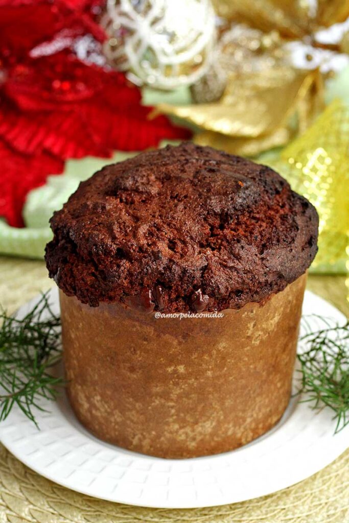 Panetone de chocolate em uma forminha de panetone, ao fundo enfeites de natal