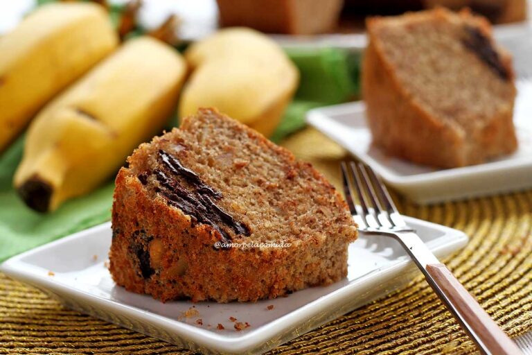 RECEITA DE BOLO DE BANANA SIMPLES DE LIQUIDIFICADOR dois pedaços de bolo de banana com pedaços de chocolate, tem três bananas ao fundo