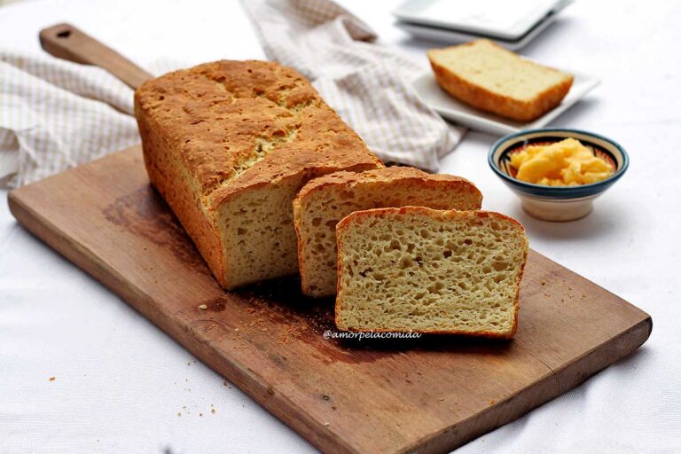 Duas fatias de pão encostadas no pão de forma, sobre tábua de madeira, ao fundo um paninho, um pote de manteiga e alguns pratinhos pequenos