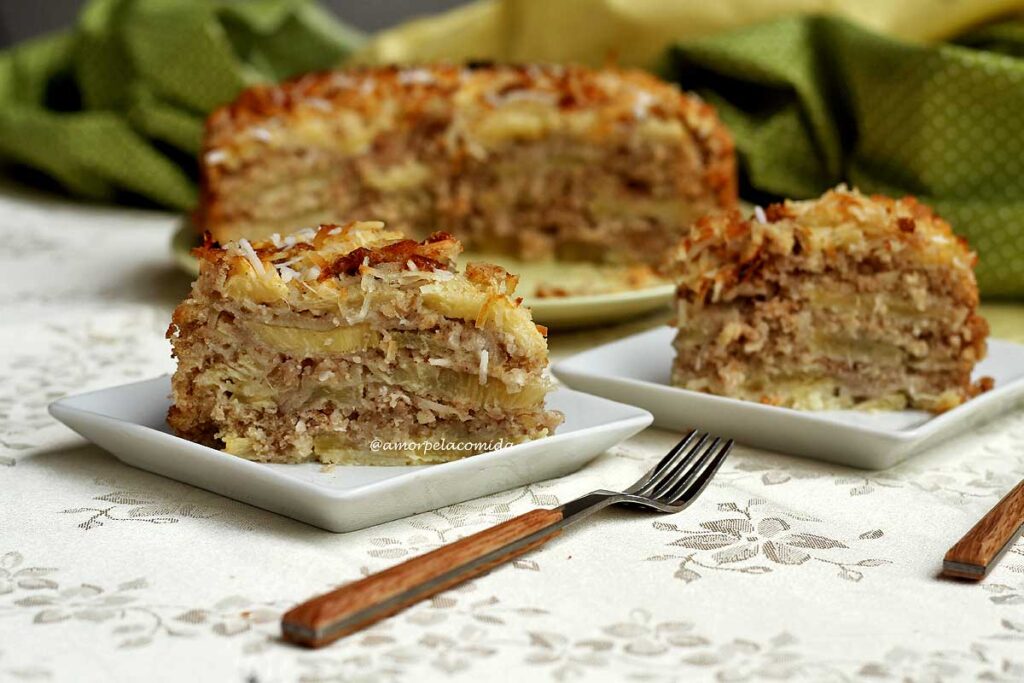 Duas fatias de torta de abacaxi com coco sobre prato quadrado pequeno, ao fundo a torta cortada