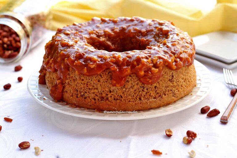 BOLO DE AMENDOIM FOFINHO DE LIQUIDIFICADOR Bolo redondo com furo no meio sobre prato branco com cobertura cremosa, caramelizada e amendoim