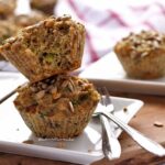 Dois bolinhos sobrepostos em um prato quadrado pequeno, o bolinho de cima está mordido, ao fundo mais bolinhos