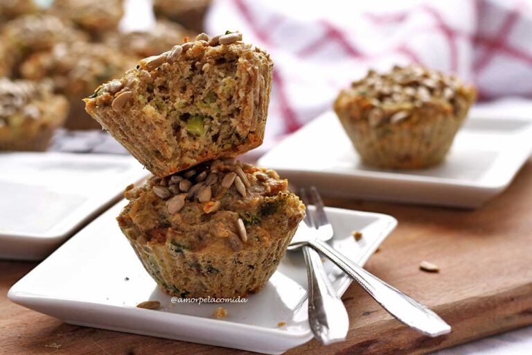 BOLO SALGADO FIT SEM GLÚTEN SEM LACTOSE Dois bolinhos sobrepostos em um prato quadrado pequeno, o bolinho de cima está mordido, ao fundo mais bolinhos