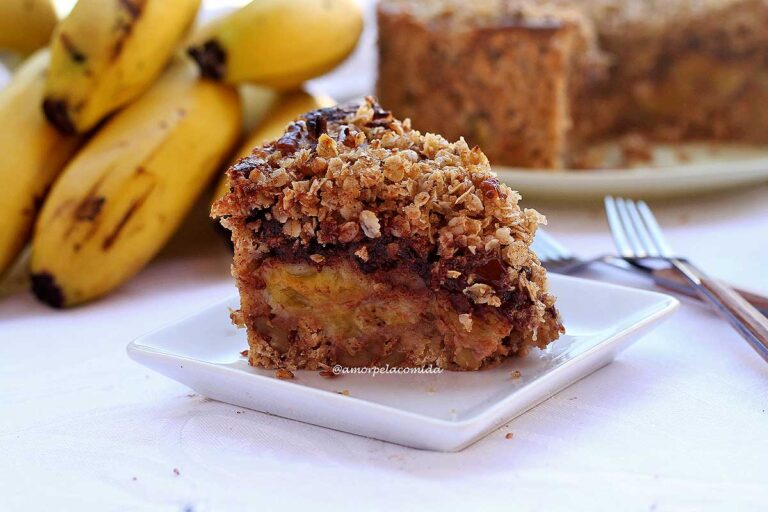 TORTA DE BANANA COM AVEIA E CHOCOLATE SEM TRIGO Fatias de torta de banana com chocolate e cobertura de flocos de aveia crocante, ao fundo algumas bananas e a torta partida