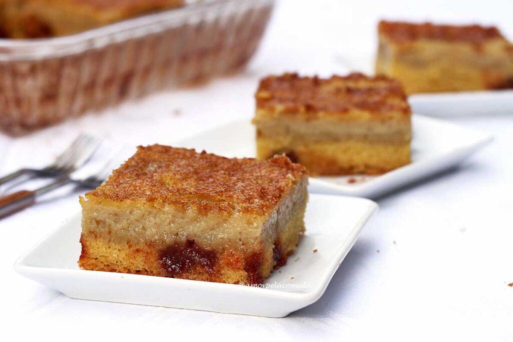 Três fatias quadradas de bolo de fubá cremoso, cada uma em um prato quadrado pequeno, elas estão alinhadas lateralmente