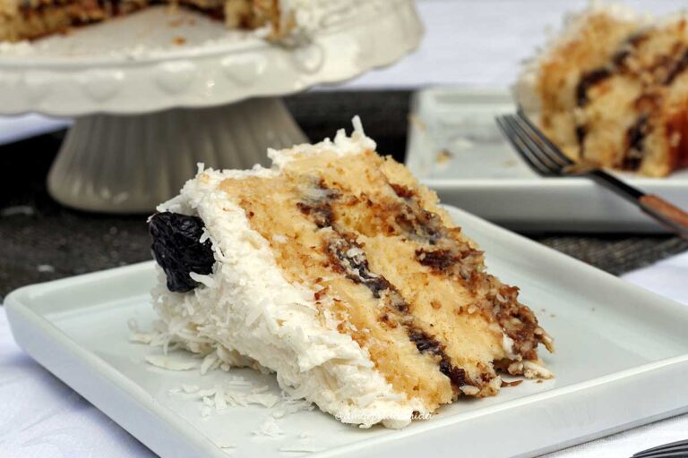 BOLO OLHO DE SOGRA SEM GLÚTEN SEM LACTOSE Fatia de bolo recheado com duas camadas de recheio, o recheio é de coco cremoso e de ameixa, a cobertura um meregue com coco e ameixa preta para decorar