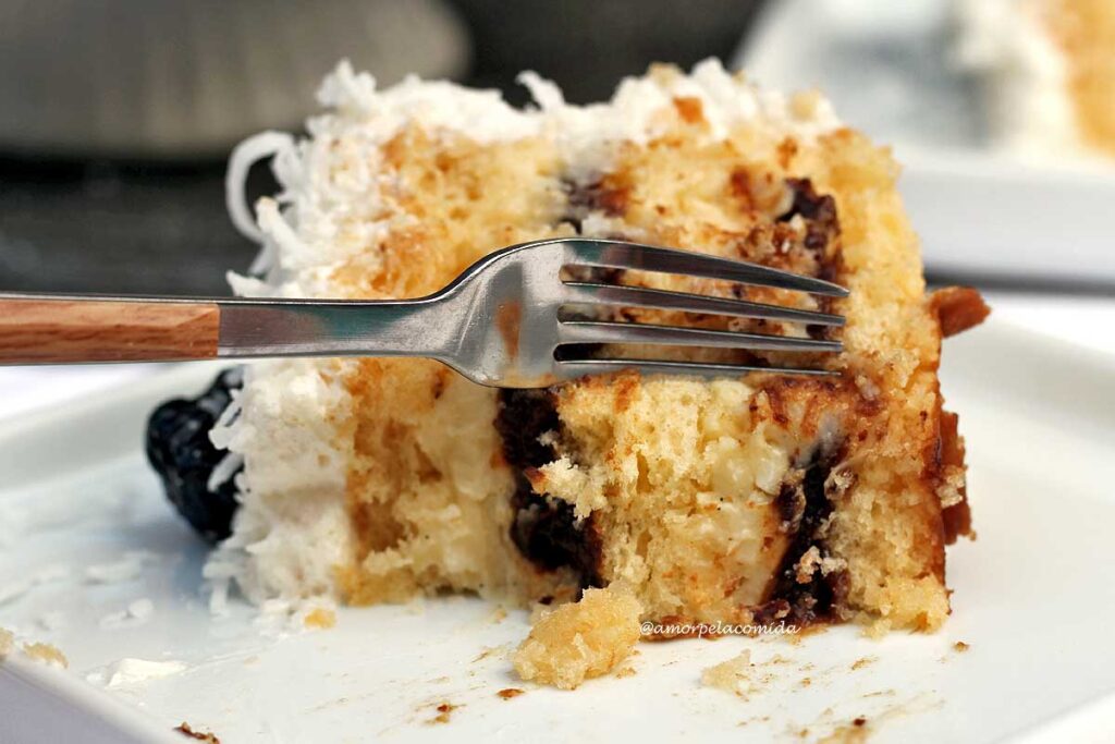 Fatia de bolo de ameixa com coco já comido e um garfo tirando um novo pedaço para ser comido