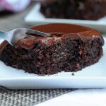 Fatia de bolo de chocolate com cobertura cremosa, tem um garfo pressionando o bolo para tirar uma segunda garfada